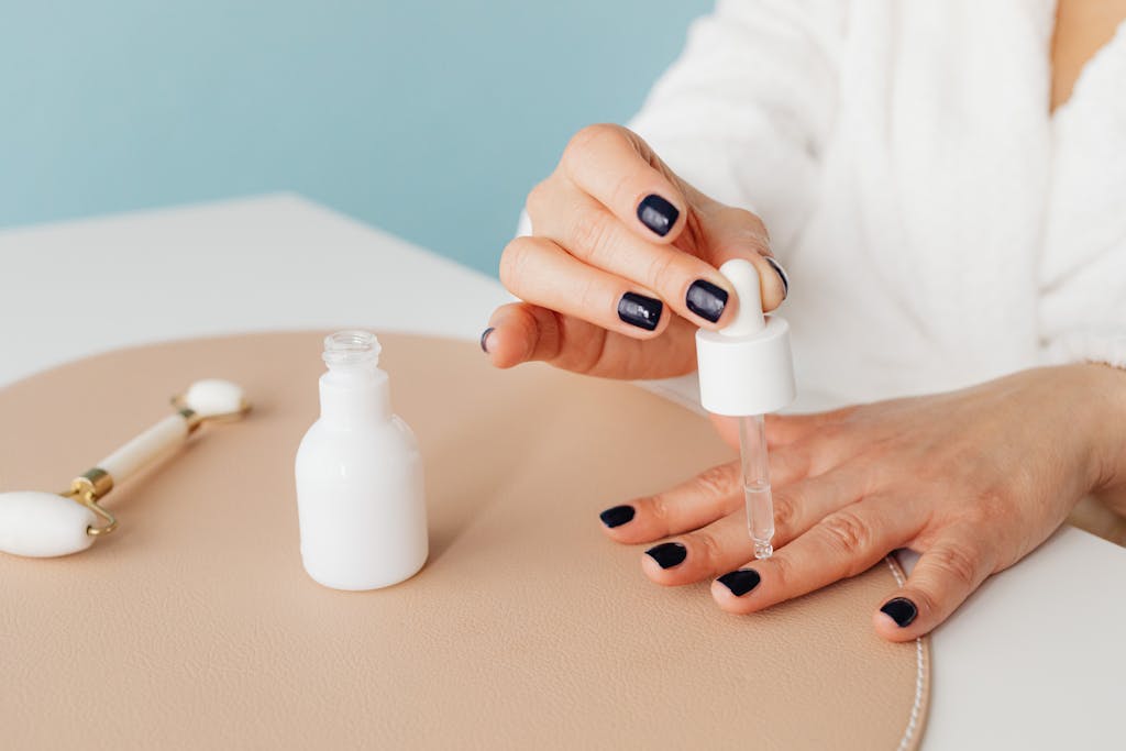 Close-up of a woman applying nail oil with a dropper for manicure care on blue background. Just one example of affordable self-care for moms. Budget friendly self-care for moms.